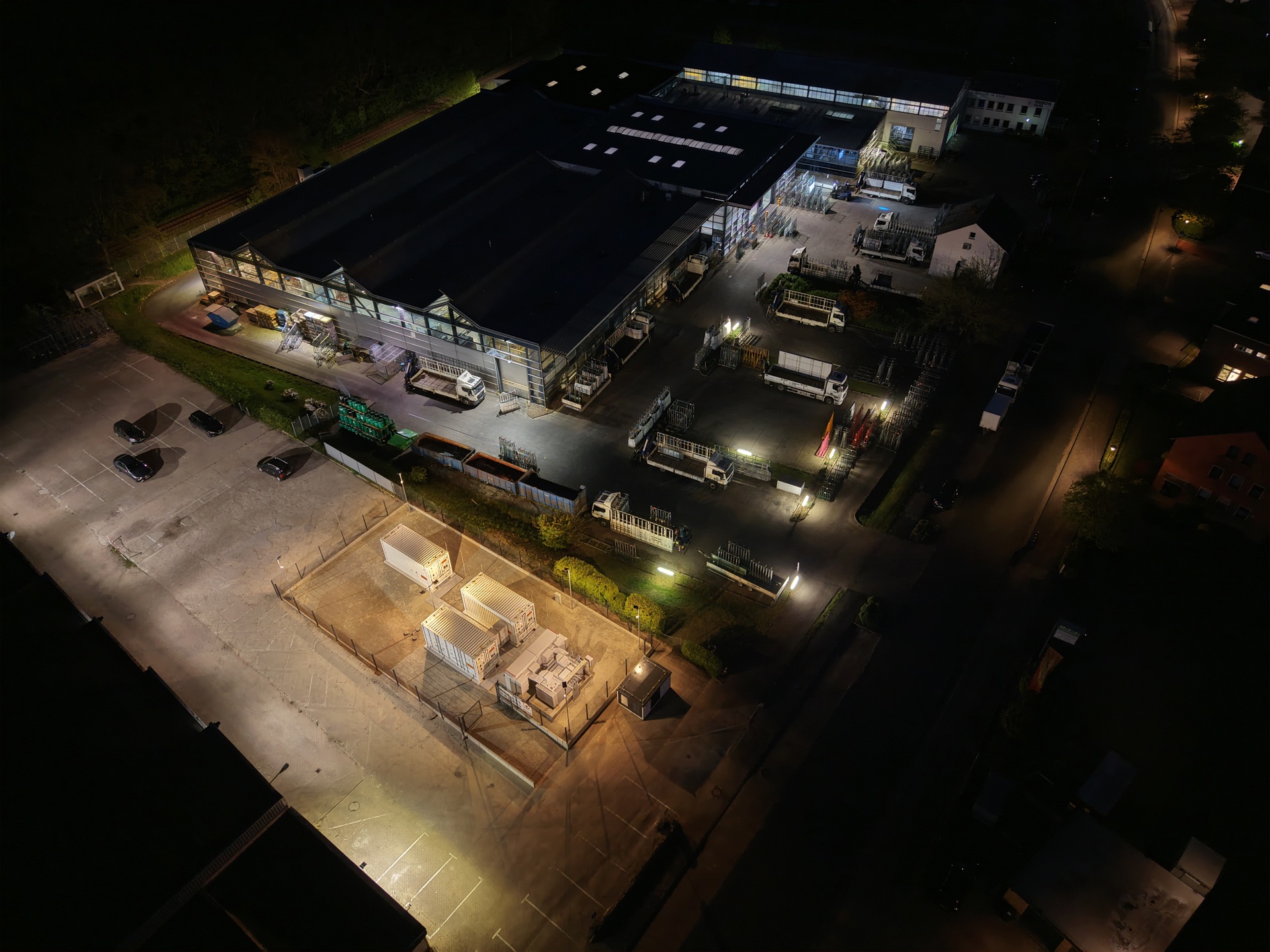 Luftaufnahme bei Nacht: Batteriespeicher-Container auf dem umzäunten Areal eines Industriebetriebs